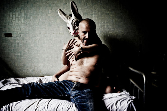 Halbnackter Mann wird auf einem Bett von einem Menschen mit Hasenkostüm im Arm gehalten