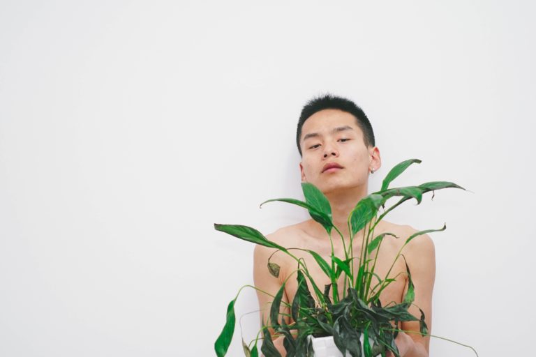 Junger Mann mit nacktem Oberkörper, der eine Pflanze hält (Photo by Palon Youth on Unsplash)