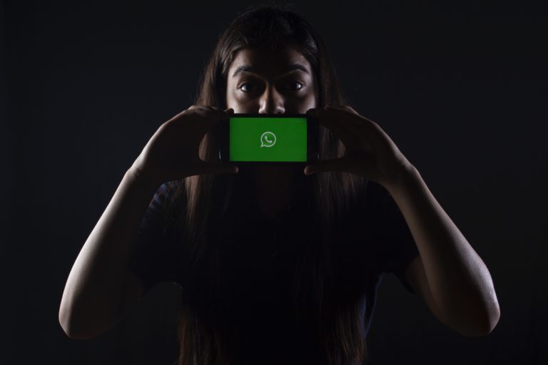 Frau hält sich ein Handy mit dem WhatsApp-Logo vor den Mund (Photo by Rachit Tank on Unsplash)