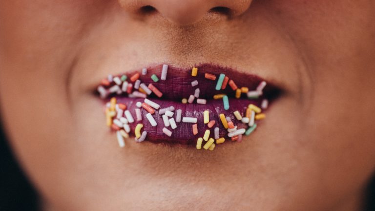 Lippen, auf denen bunte Zuckerstreifen kleben (Photo by Constantinos Panagopoulos on Unsplash)